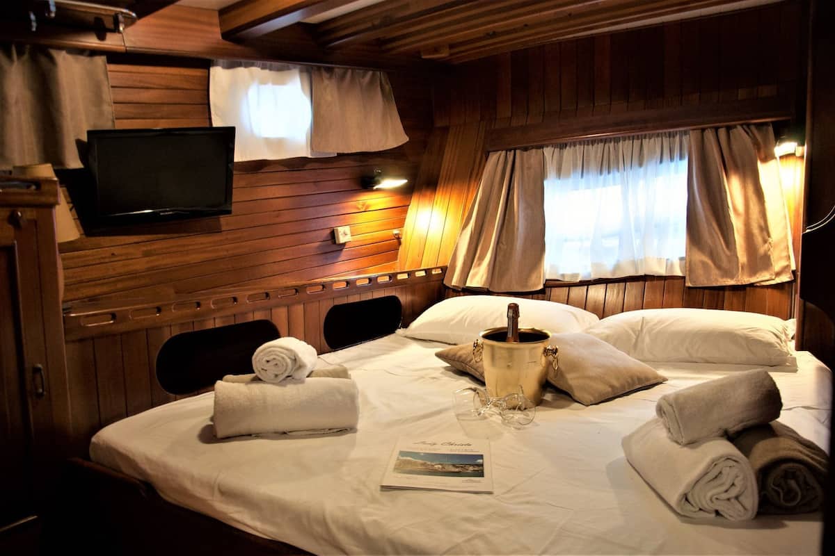 A cozy cabin-style room with a wooden interior, a flat-screen TV mounted on the wall, a bed with neatly folded towels, a bucket of champagne, and a book on the bed.