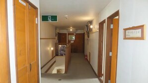 A narrow hallway with wooden doors and a green emergency exit sign. - Rental Lodge WHITE RABBIT Madarao kogen Cottage MIDORINO KAZE (Iiyama)