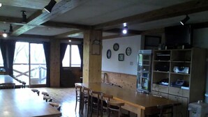 A rustic interior with a wooden dining table, bar stools, a refrigerator, and a television on a shelf. - Rental Lodge WHITE RABBIT Madarao kogen Cottage MIDORINO KAZE (Iiyama)