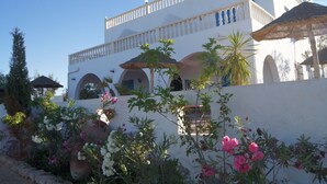 A white building with arches and a balcony. There are potted plants and flowers in the foreground. - Domaine El-Manar (Zarzis)