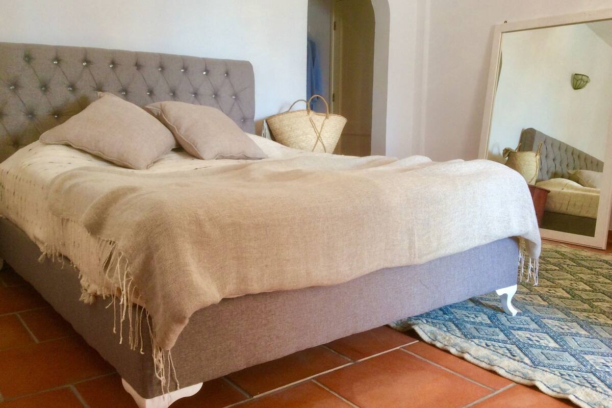 A bed with a tufted headboard, a beige blanket, and a woven throw.