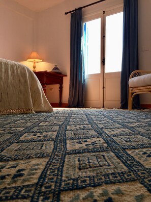 Una habitación con una cama grande, una mesita de noche con lámpara y una silla.