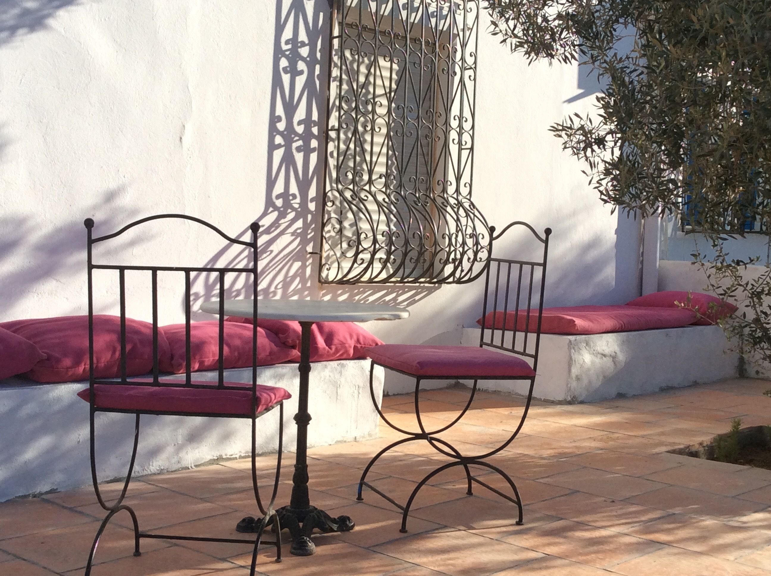 A patio with a metal table and chairs, a white wall, and a decorative window grille.