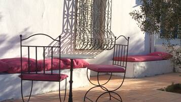 A patio with a metal table and chairs, a white wall, and a decorative window grille.