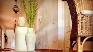 A hallway with a patterned carpet, a wicker chair, and two white vases with plants. - Domaine El-Manar (Zarzis)