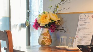 A wooden desk with a vase of flowers, a menu, and a chair. - La Curandera (Rosta)