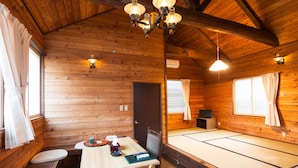 A wooden cabin interior with a dining table, benches, a futon bed, and a ceiling light fixture. - Condominium Hotel Naeba West (Yuzawa)