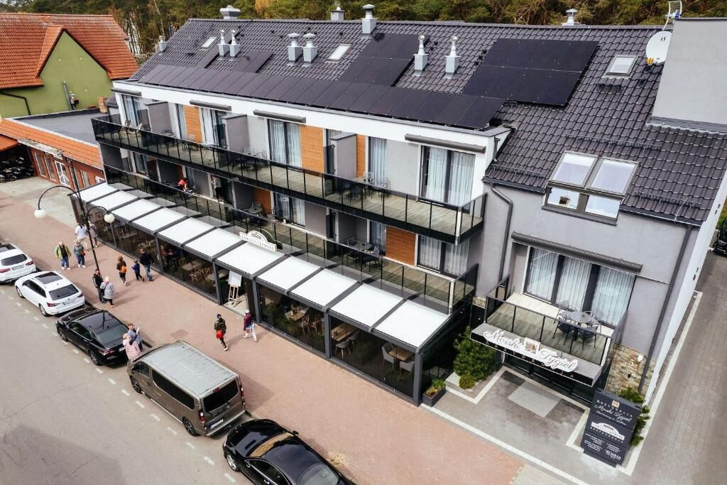 A modern multi-story hotel with a glass facade, outdoor seating area, and a restaurant.