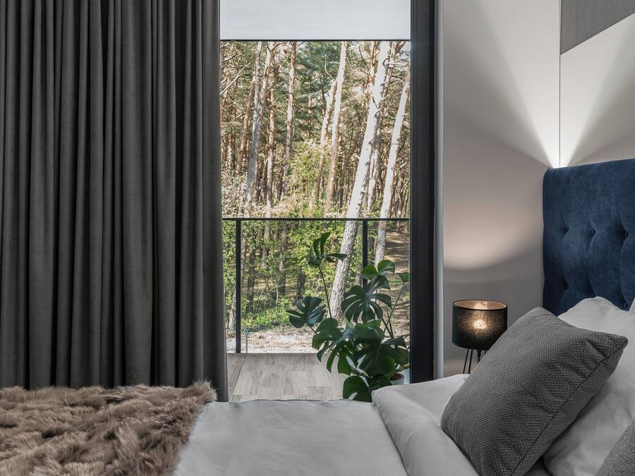 A bedroom with a large window, a bed with white bedding, a blue headboard, and a plant.