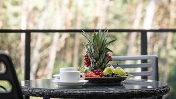 Une table ronde avec un bord tressé, une tasse et une soucoupe blanches, un saladier rempli d’ananas, de baies et de poires, et une chaise avec un cadre noir.