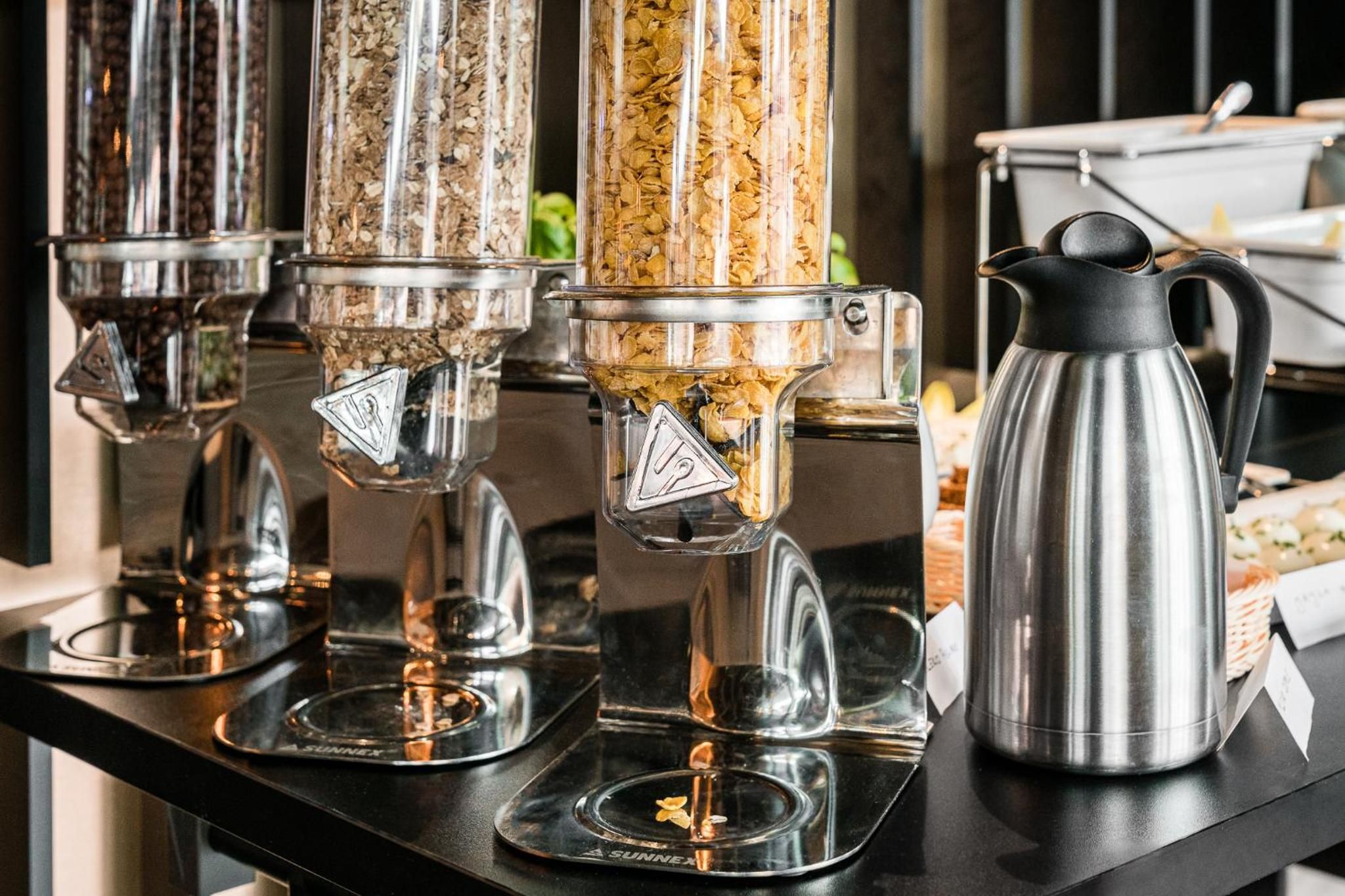 Un comptoir de cuisine avec une machine à café et trois distributeurs en verre remplis de différents types de céréales ou de grains.