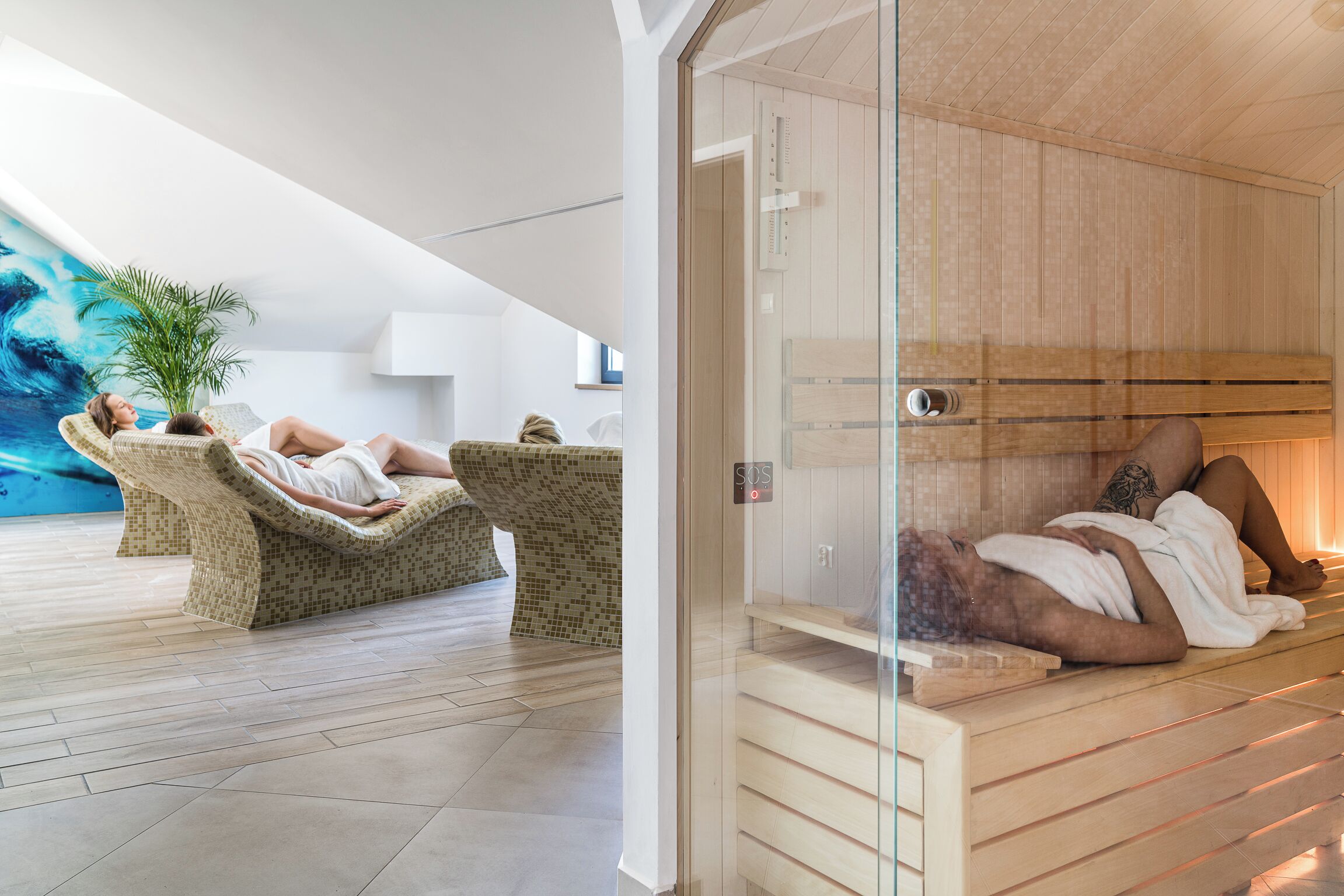 Un moderno espacio de spa con una sauna de cristal, un área de relajación con sillas de mimbre y un cuadro abstracto de gran tamaño en la pared.