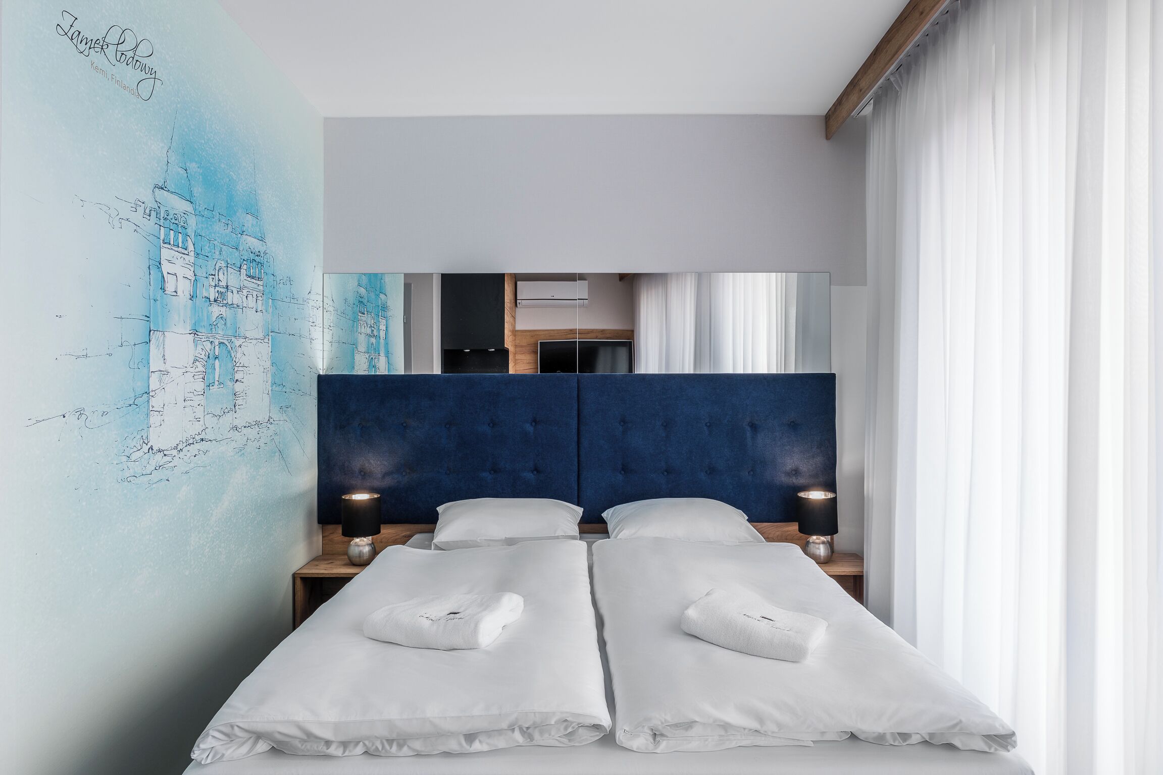Una habitación de hotel moderna con una cama grande, cabecero, lámparas de noche y una obra de arte en la pared.