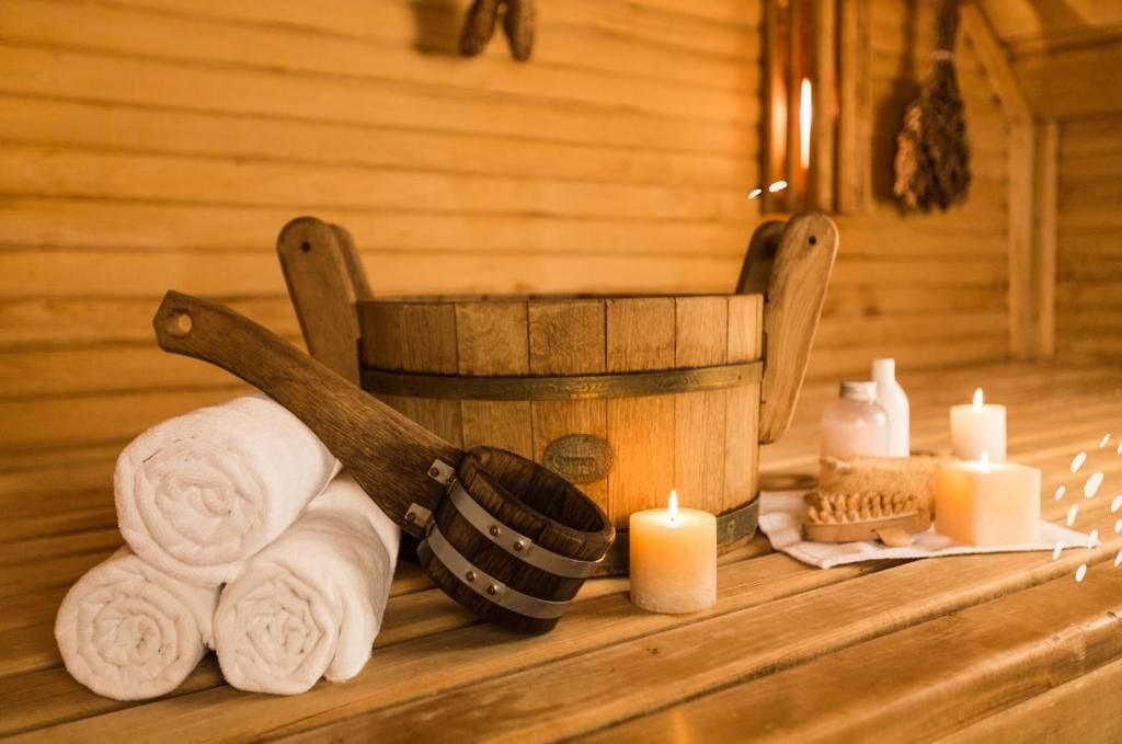 Una bañera de madera, toallas enrolladas, un cubo de madera y velas sobre un suelo de madera.