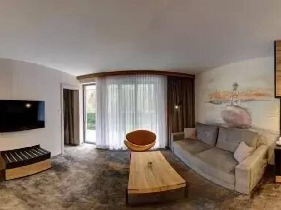Een moderne woonkamer met een flatscreen televisie, een houten salontafel, een bank en een klein zithoekje met een schaal.