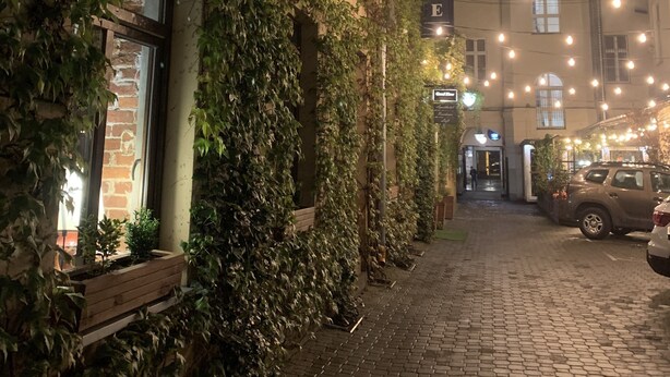 A nighttime street view with a building covered in ivy, a sign reading "GOOD TIME," and string lights. - Loft Piotrkowska by Good Time (Lodz)
