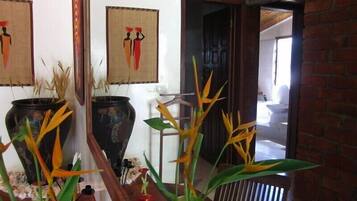 A room with a brick wall, a wooden door, and a window. There are two large vases with plants on a table.