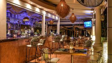 Uma área de bar com balcão, banquetes e uma tela de televisão.