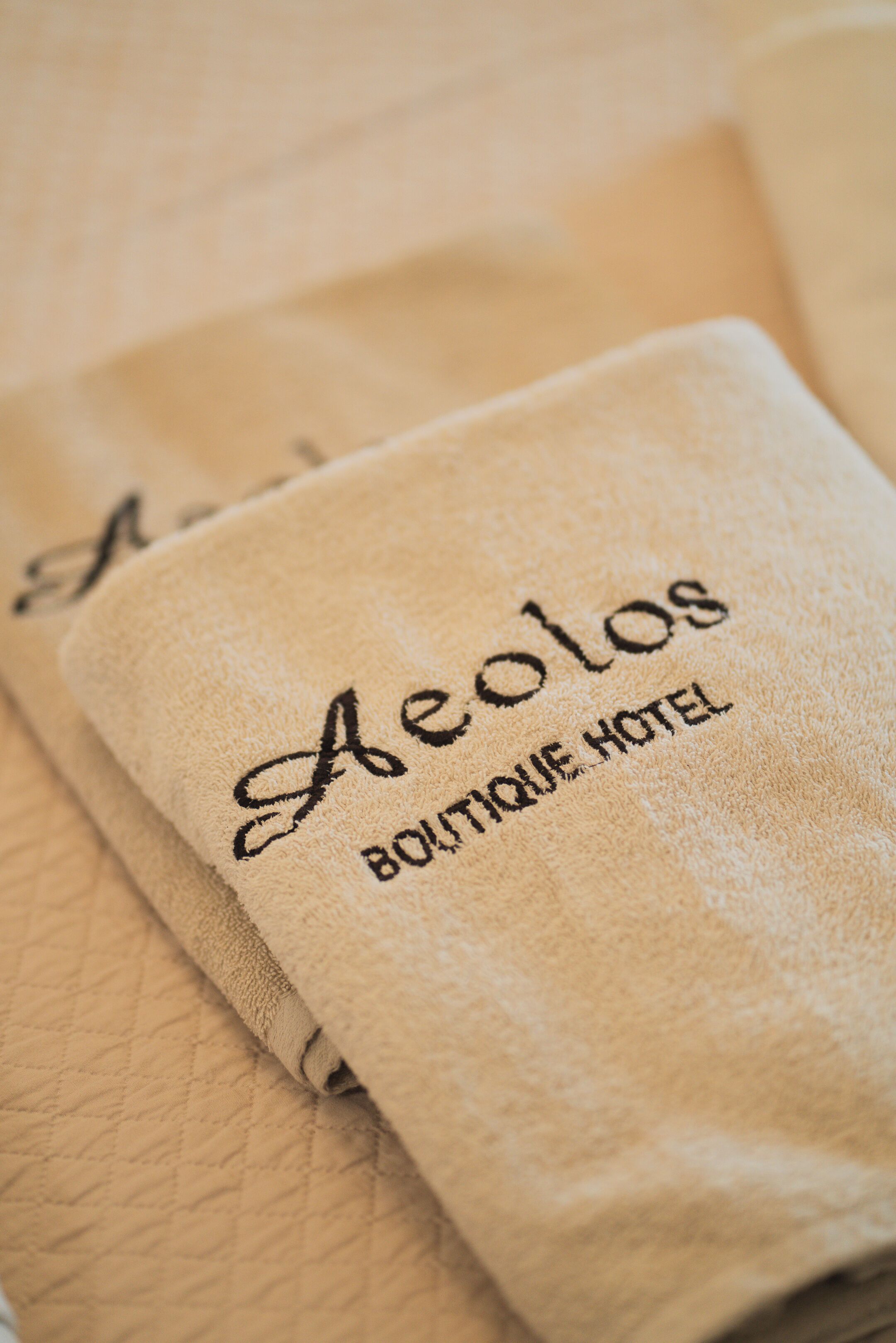 A folded beige towel with embroidered text reading "Aelos Boutique Hotel."