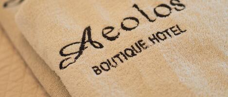 A folded beige towel with embroidered text reading "Aelos Boutique Hotel."