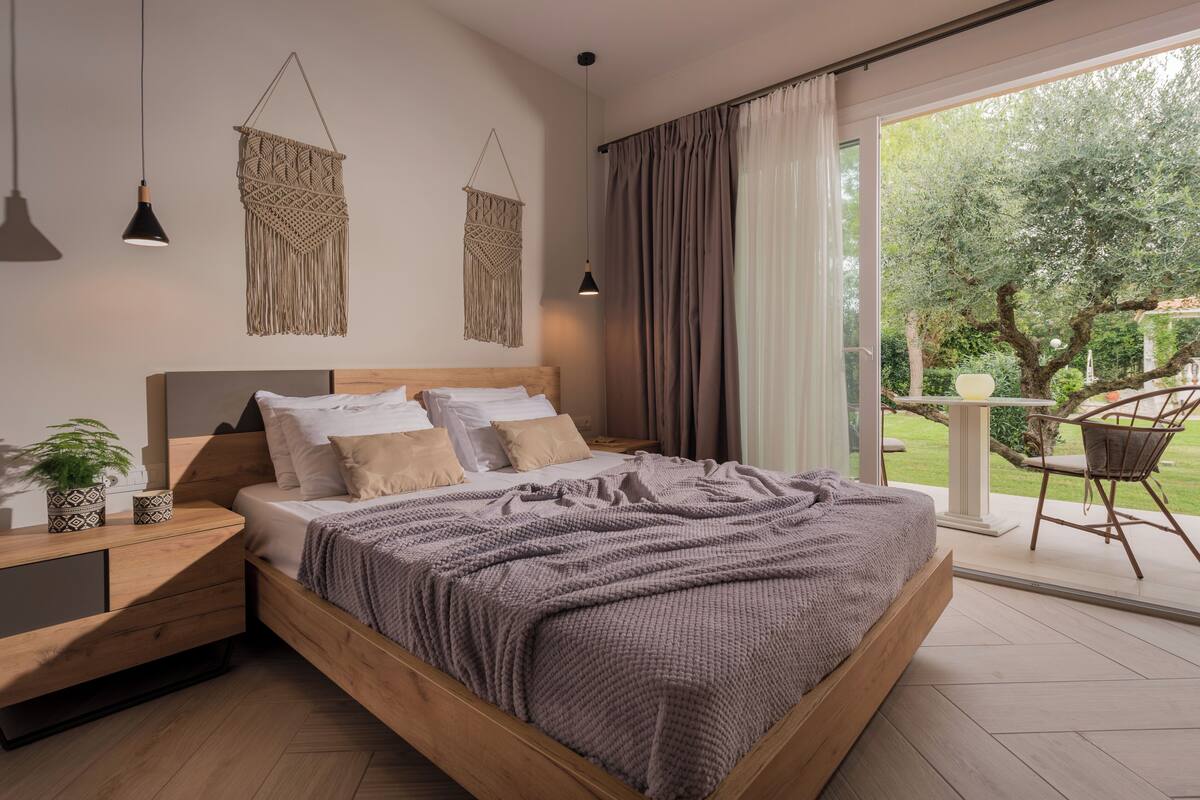 Una camera da letto moderna con un letto in legno, decorazioni macramè alle pareti e vista sul giardino attraverso ampie finestre.