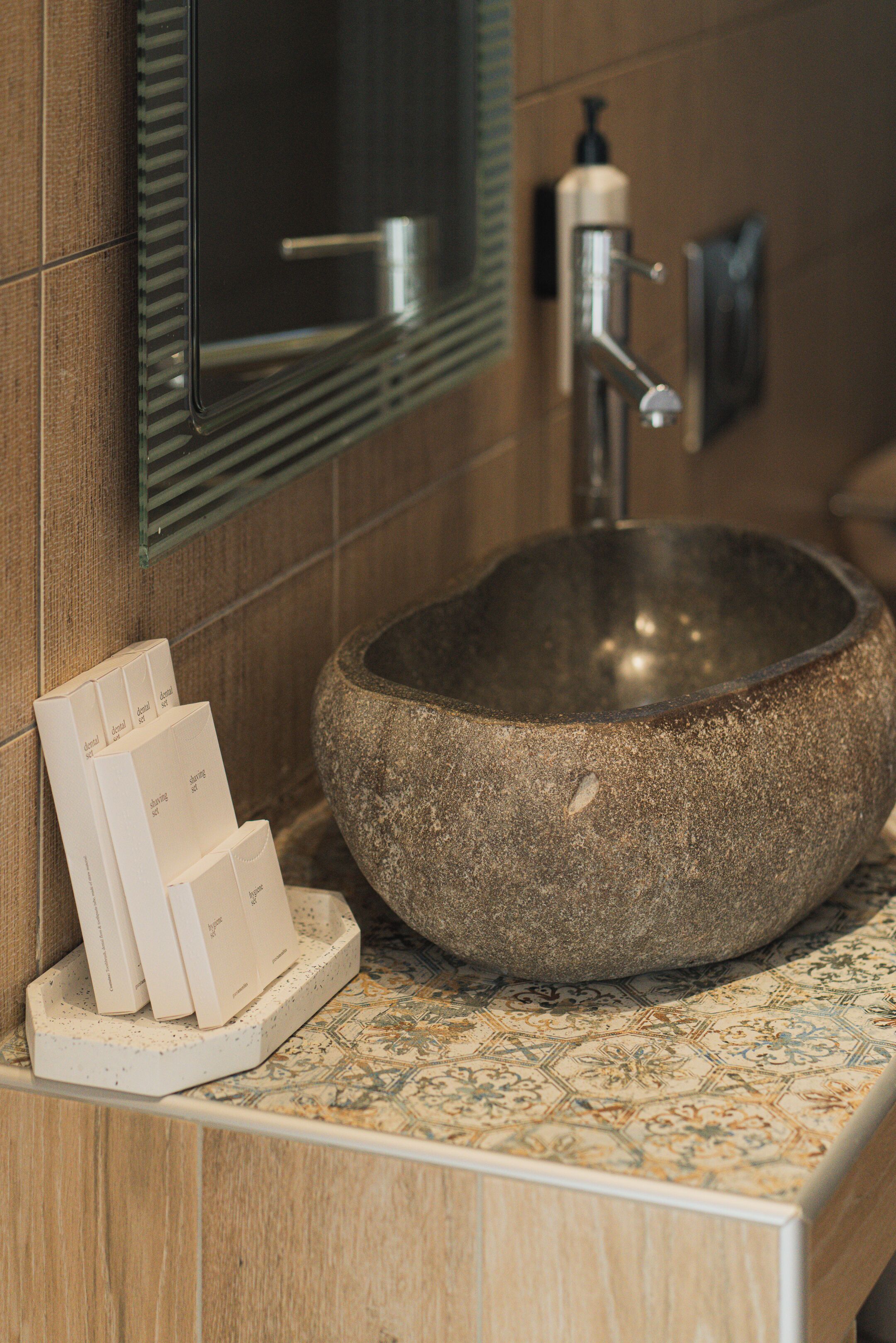 A stone basin sink with a soap dispenser, a mirror, and a tiled countertop.