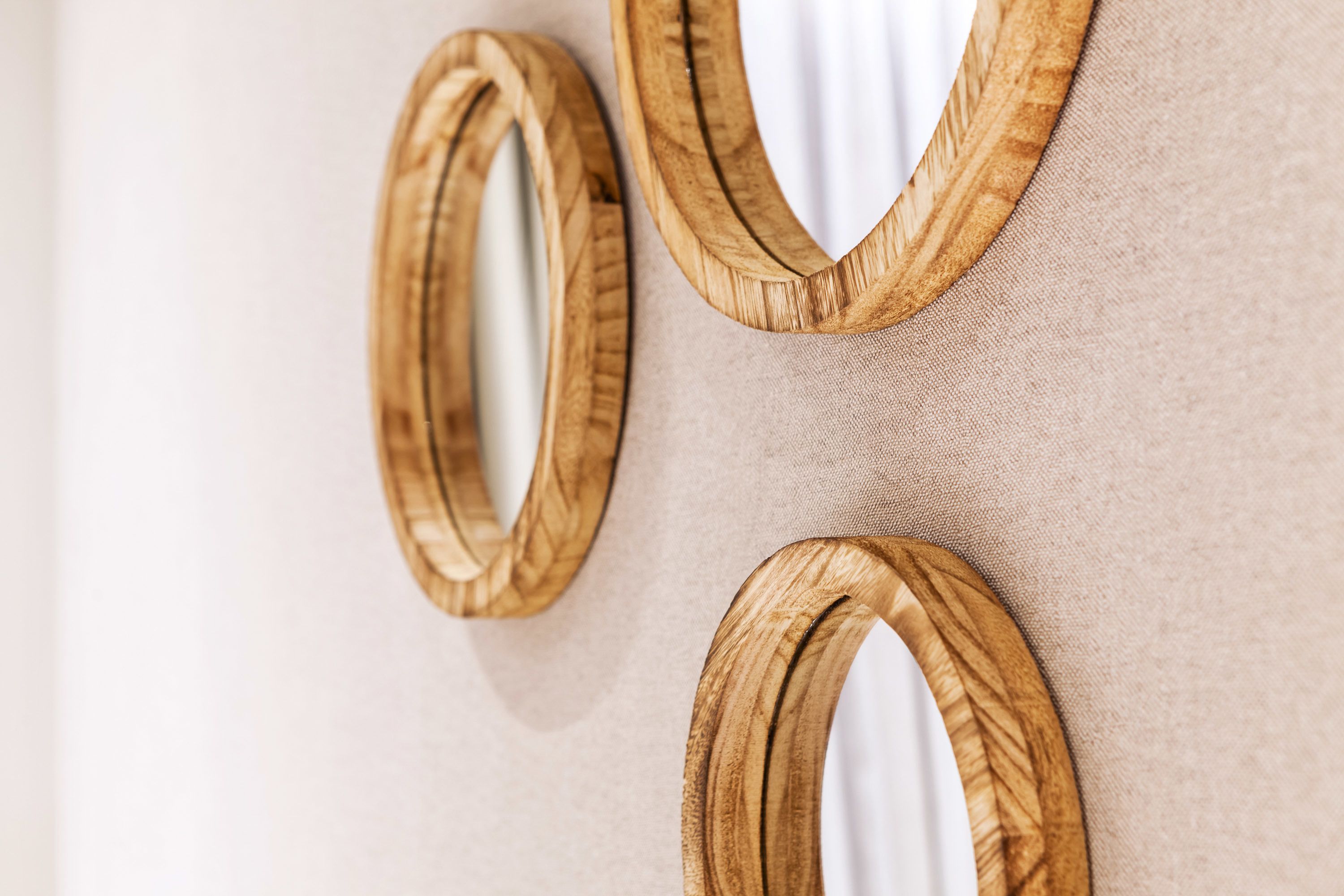 Three wooden-framed mirrors on a beige wall.