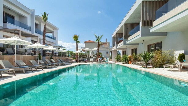 A modern hotel with a large swimming pool, sun loungers, and palm trees.