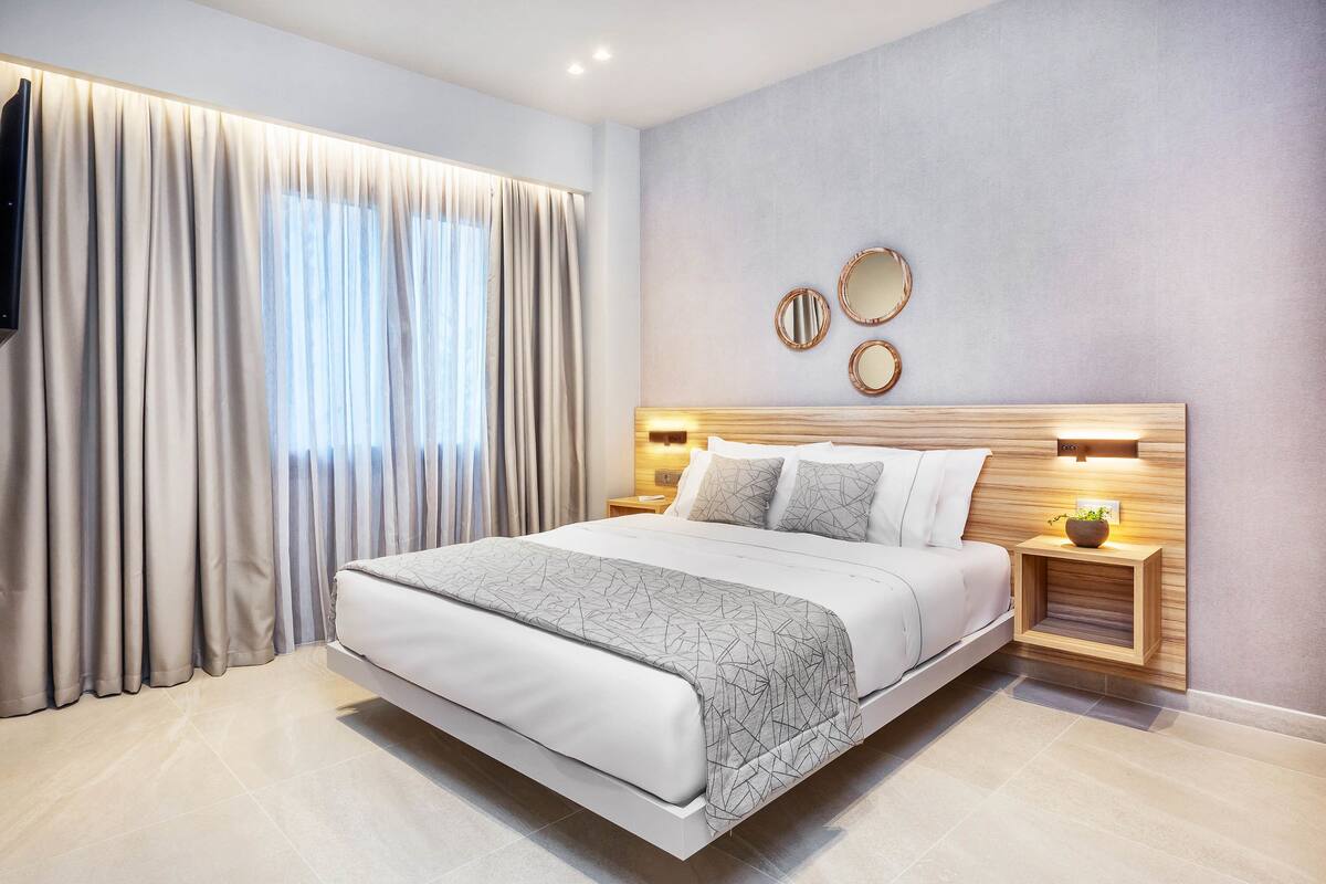 A modern bedroom with a large bed, a bedside table with a lamp, and a wall-mounted mirror.