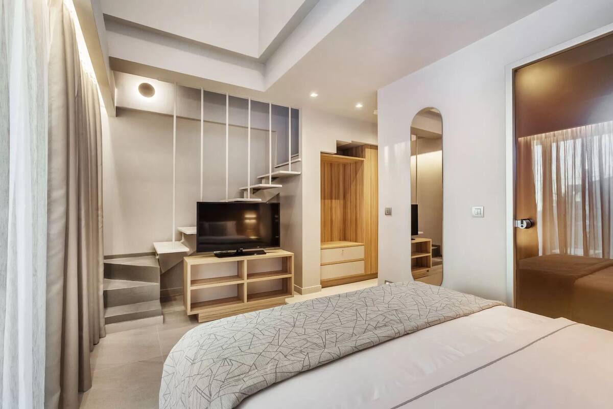 A modern bedroom with a bed, TV, built-in shelving, and a staircase.
