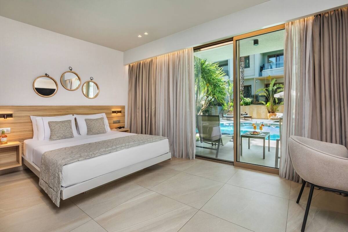 A modern hotel room with a large bed, a glass door leading to a pool area, and a view of the outdoors.