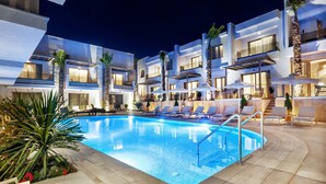 A modern hotel with a swimming pool, lounge chairs, and palm trees.