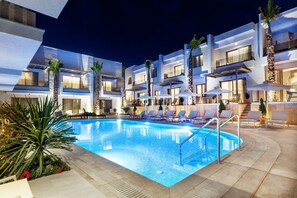 A modern hotel with a swimming pool, lounge chairs, and palm trees. - Pefki Deluxe Residences (Kassandra)