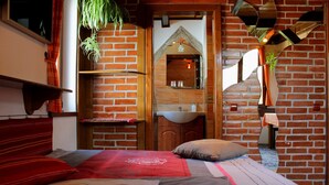 A bedroom with a brick wall, a wooden door, a bed with a red and grey bedspread, and a hanging plant. - Casa Crina (Saliste)