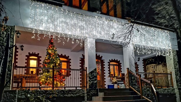 A building with a staircase leading to a porch, decorated with string lights and a Christmas tree. - Casa Crina (Saliste)