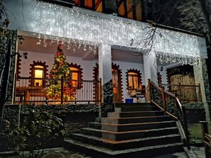A building with a staircase leading to a porch, decorated with string lights and a Christmas tree. - Casa Crina (Saliste)