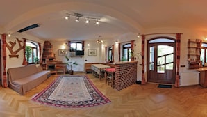 A spacious living room with a wooden herringbone floor, a sofa, a dining table, and a fireplace. - Casa Crina (Saliste)
