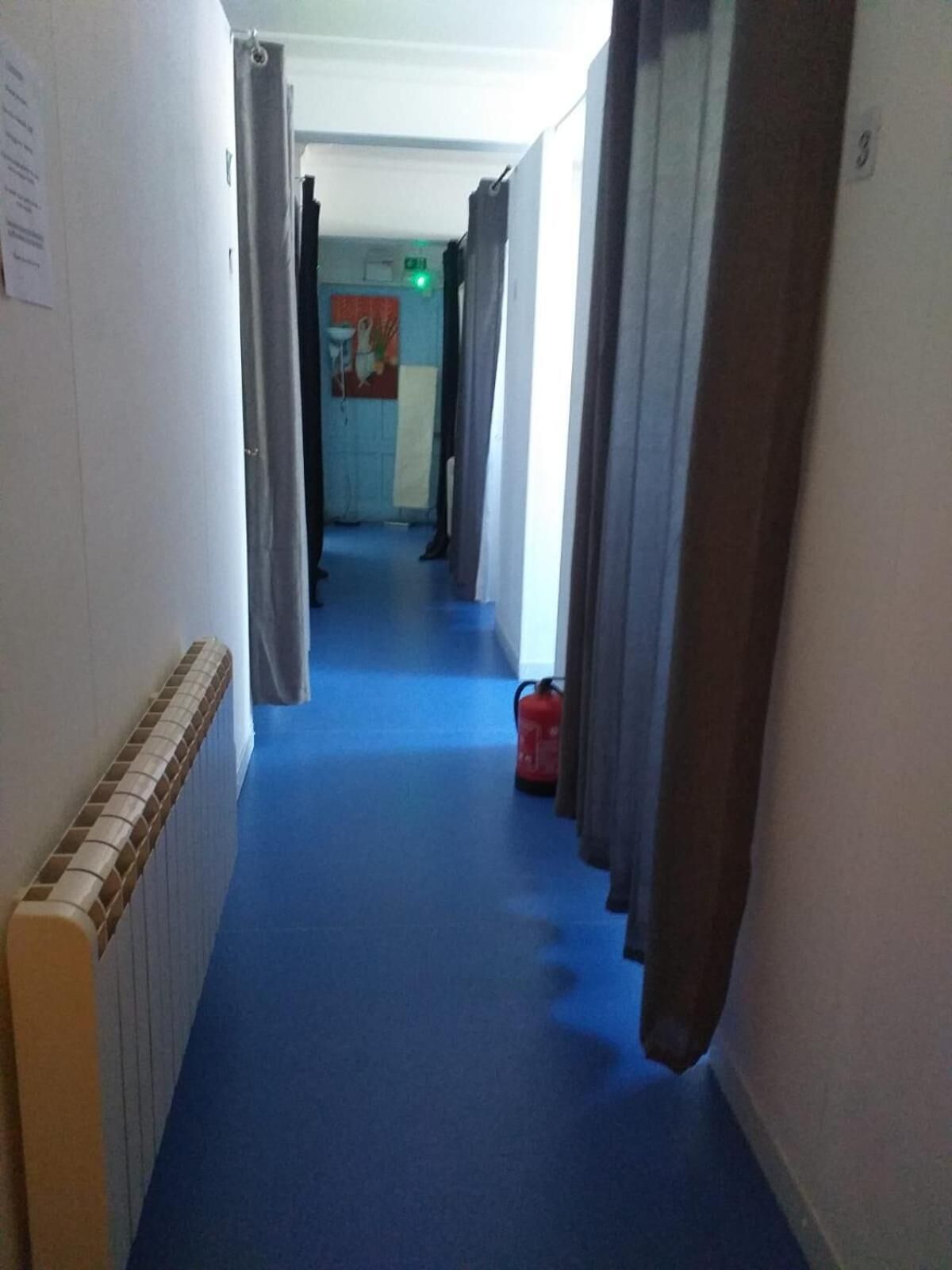A hotel corridor with blue carpet, curtains, and a fire extinguisher.