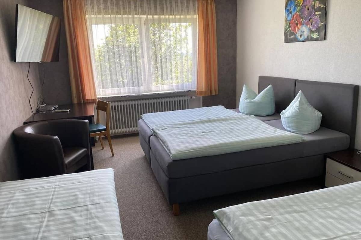 Una habitación de hotel con una cama, dos mesitas de noche, un escritorio, una silla y una ventana con cortinas.