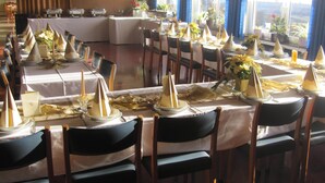 Un comedor con mesas dispuestas para un evento formal, con manteles blancos, servilletas doradas y sillas oscuras.