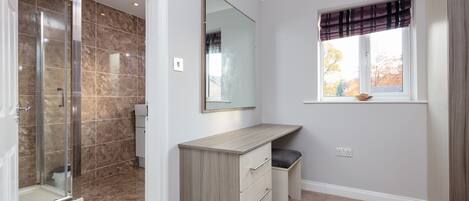 A bathroom with a shower, a vanity with drawers, a mirror, and a window with a view of trees.