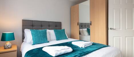A neatly made bed with a teal throw blanket, a bedside lamp, and a wooden nightstand.