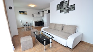 Een moderne woonkamer met een glazen salontafel, een bank en een eetgedeelte met tafel en stoelen.