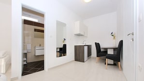 Een moderne badkamer met toilet, wastafel en spiegel. Er staat een klein tafeltje met twee stoelen en een vaas met bloemen. De kamer heeft witte wanden en een betegelde vloer.