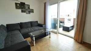 Een moderne woonkamer met een hoekbank, een glazen salontafel en een schuifpui naar een buitenruimte.