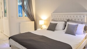 A neatly made bed with a grey and white color scheme, a bedside lamp, and a window with curtains. - Cosy S3 At Sidi Bou Said Village (Sidi Bou Said)
