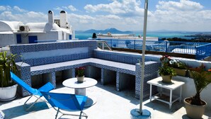 A rooftop terrace with a blue umbrella, a seating area with a table, and potted plants. - Cosy S3 At Sidi Bou Said Village (Sidi Bou Said)