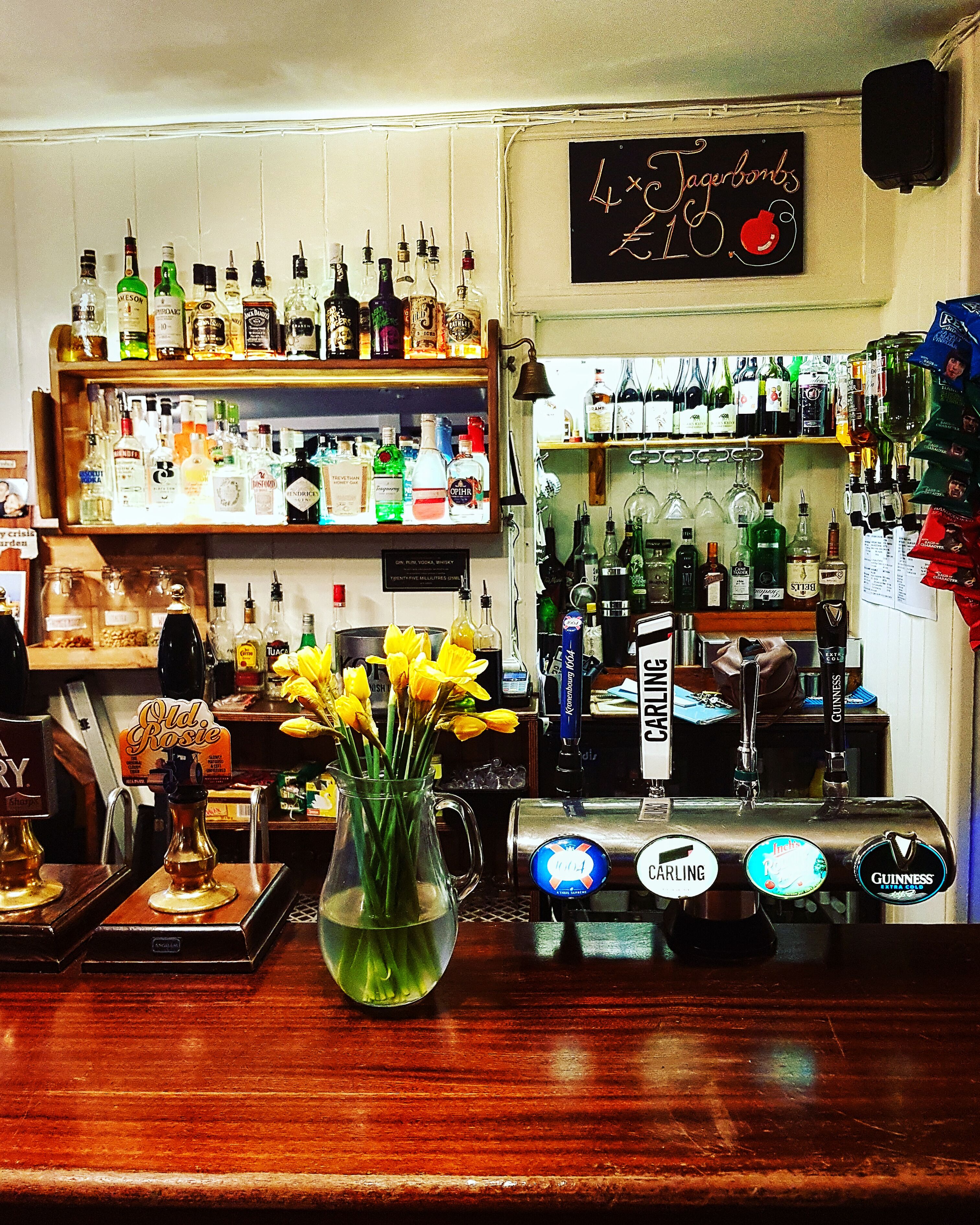 Un bar con diverse bottiglie di liquore, un rubinetto per la birra e un cartello con la scritta 'Tagerbombs £10'.