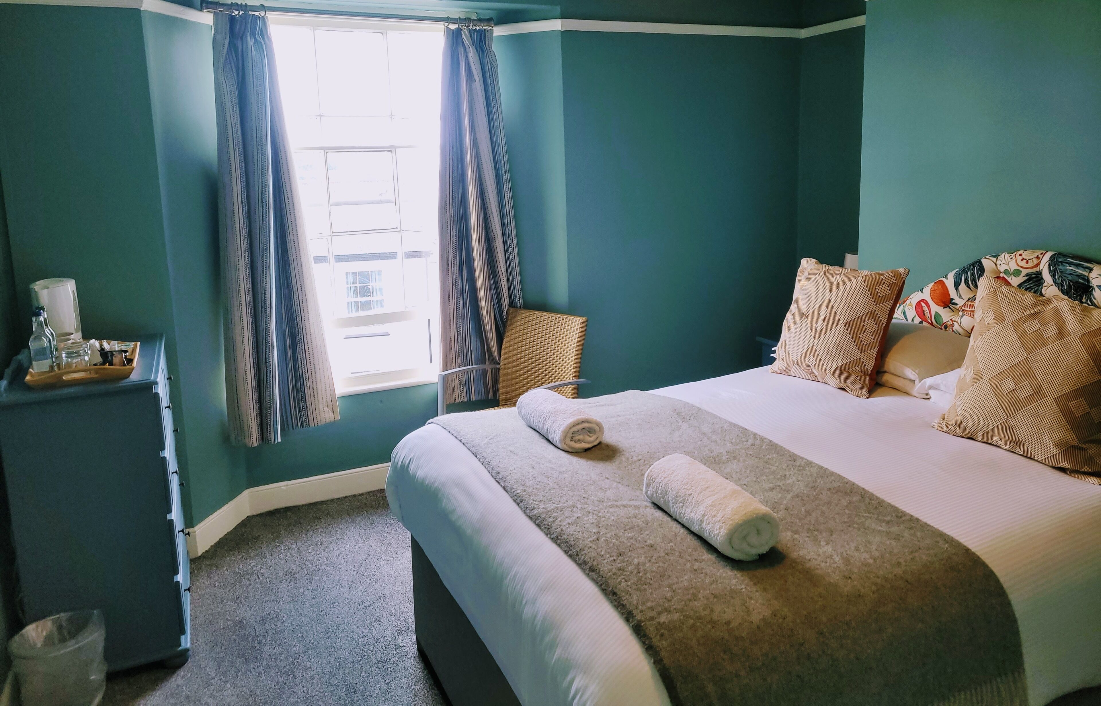A hotel room with a bed, a nightstand, a window with curtains, and a view of buildings outside.