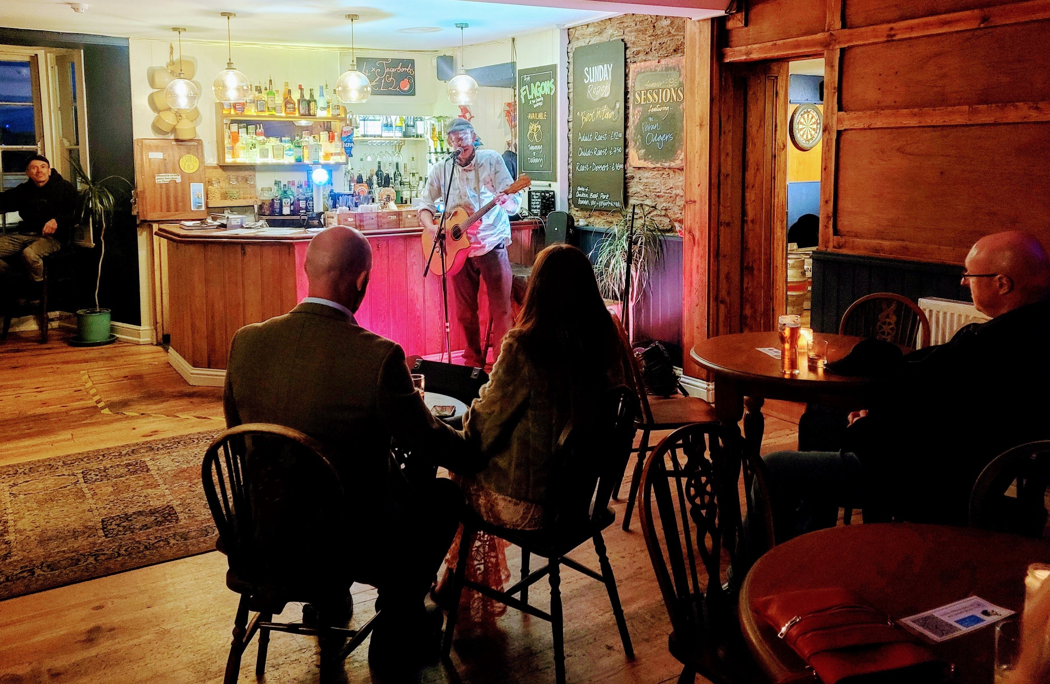 A bar area with a musician performing, wooden furniture, and a bar counter with various bottles.